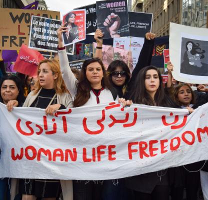 A group of Iranian women at a protest holding a white banner that reads "Woman, Life, Freedom" in red. | Photo by: Viktoria Bykanova/Shutterstock