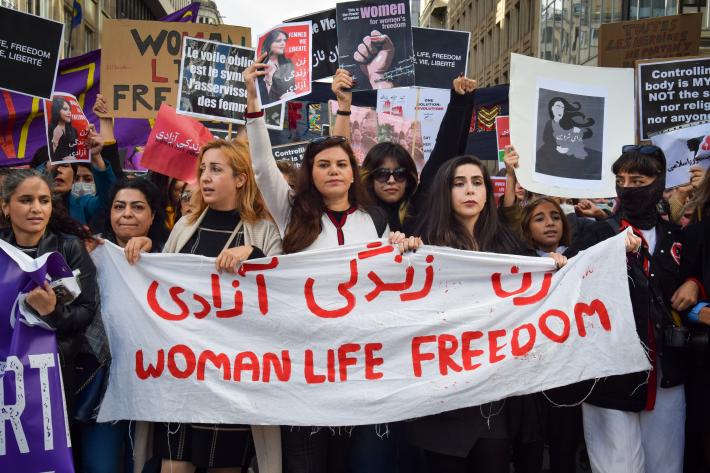 A group of Iranian women at a protest holding a white banner that reads "Woman, Life, Freedom" in red. | Photo by: Viktoria Bykanova/Shutterstock