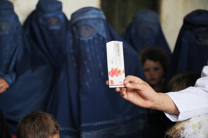 A midwife holds a medicine pack as the community members look on.